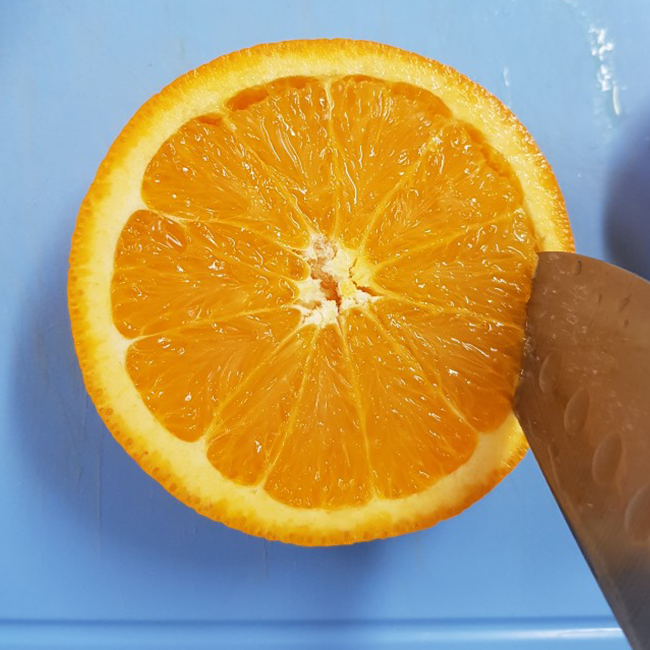 大きいオレンジの中身を切り抜きます。おしりを下に置いて包丁を刺し切り進めます。