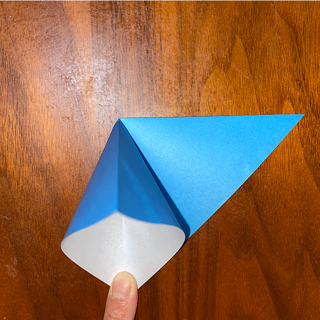 上の紙１枚を持って開き、上の角と下の角を合わせて潰して折る。